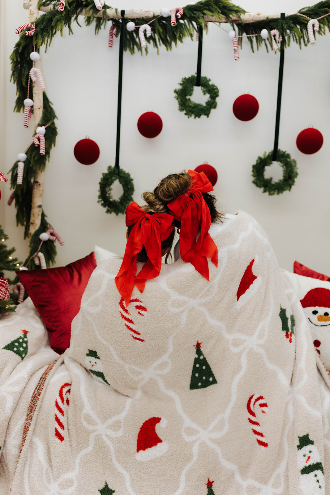 Woman and child sitting on a bed with a Christmas-themed blanket and decorations.