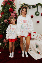 Two people wearing matching Christmas-themed sweaters in a festive setting with a decorated tree.