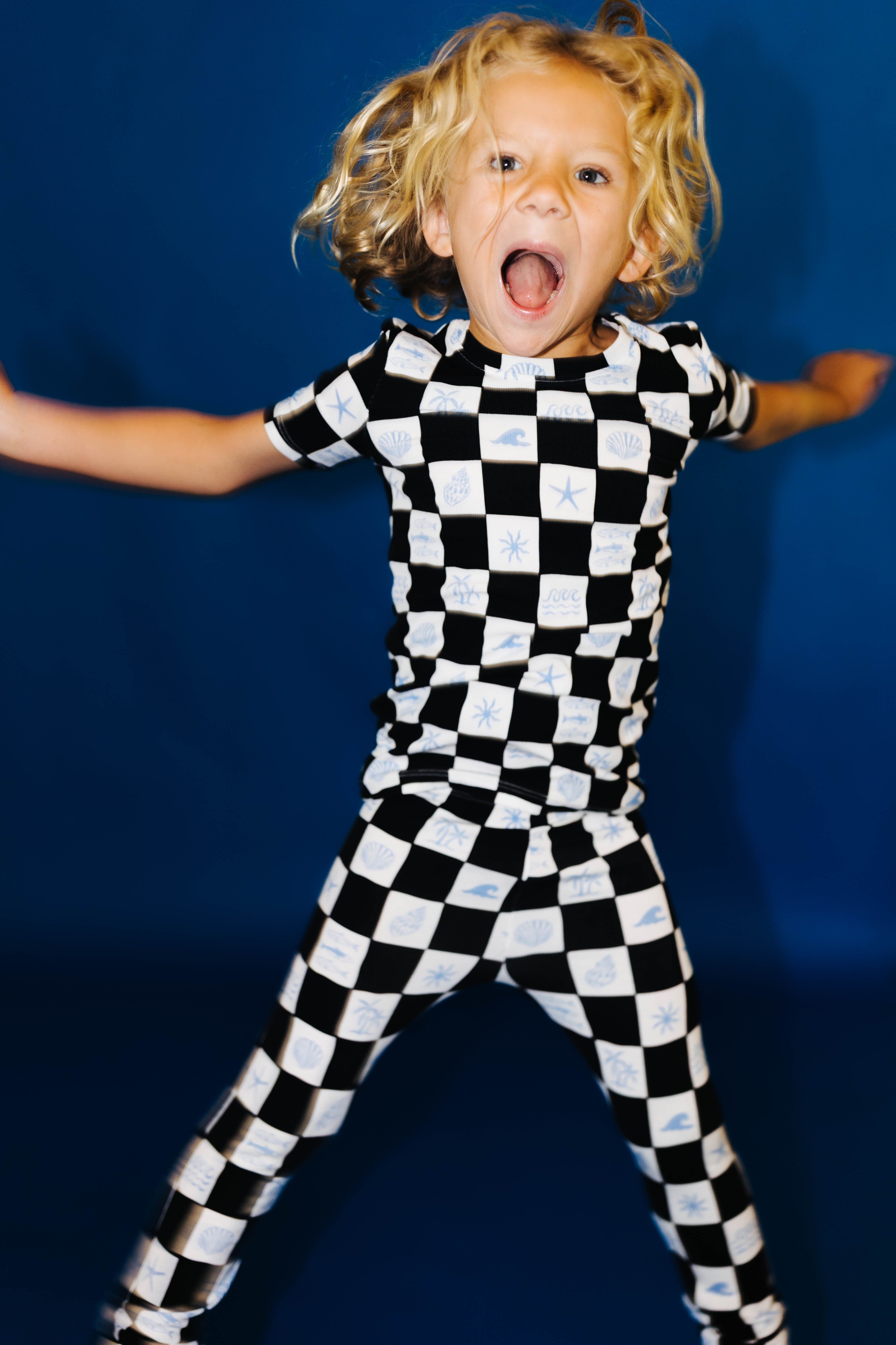 Child wearing a black and white checkered pj against a blue background smiling really big