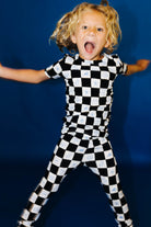 Child wearing a black and white checkered pj against a blue background smiling really big