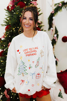 Woman wearing a white sweater with Christmas-themed designs in front of a decorated Christmas tree.