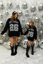 Mother and daughter smiling at each other in matching sweatshirts in front of a new year's background