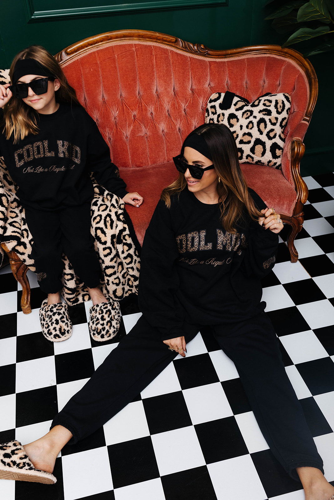 Two women sitting on a red couch with leopard print accents on a black and white checkered floor.