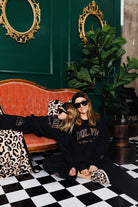 Two people sitting on a checkered floor with a green wall and decorative mirrors.