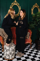 Two women in black outfits standing in a room with gold mirrors and a checkered floor.
