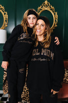 Two people wearing matching black sweatshirts with text, standing in a room with decorative mirrors.