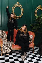Two women posing on a checkered floor with a green wall and decorative mirrors.