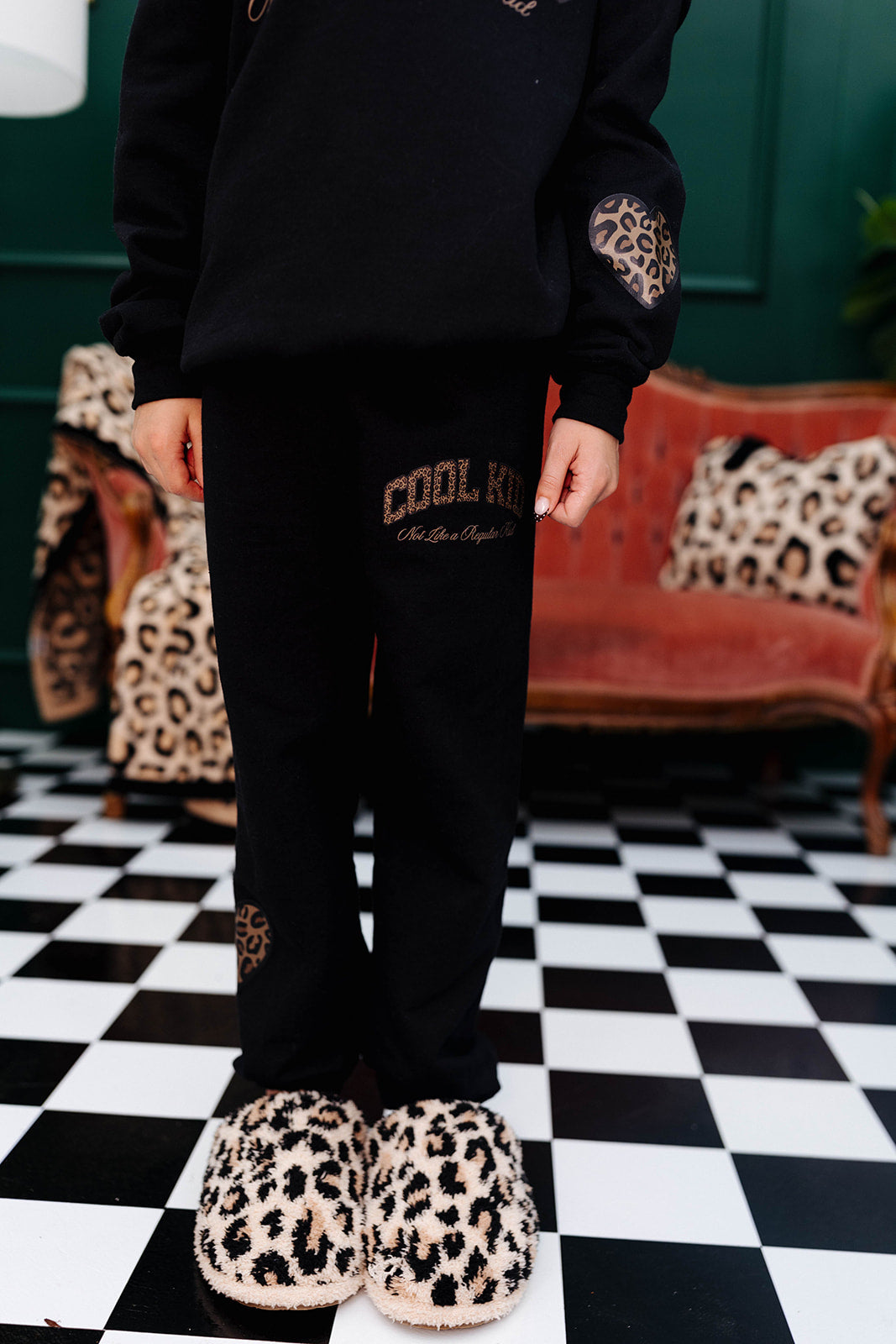 Person wearing black sweatshirt and pants with leopard print shoes on a checkered floor.