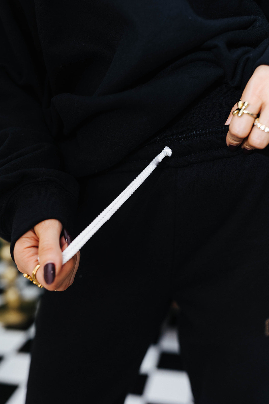 Person holding a white drawstring on black clothing and checkered floor in the background