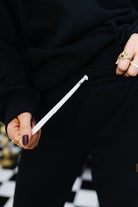 Person holding a white drawstring on black clothing and checkered floor in the background