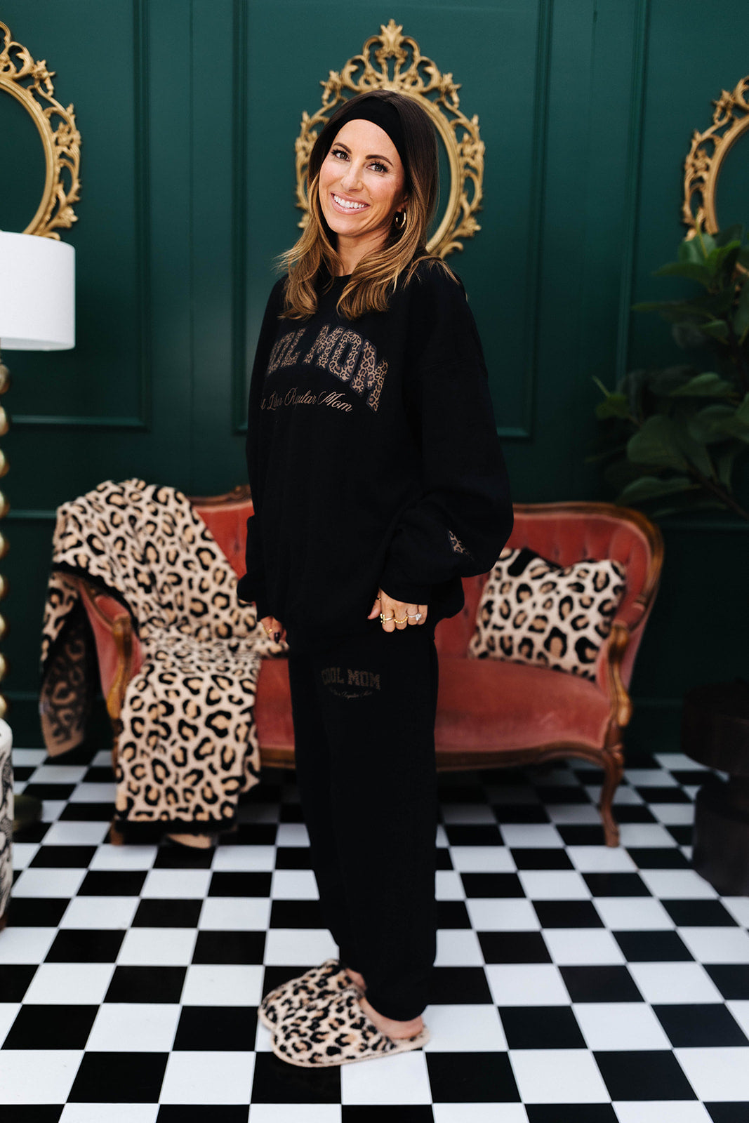 Woman in a black sweatshirt standing in a room with checkered floor, leopard print blanket, and furniture.