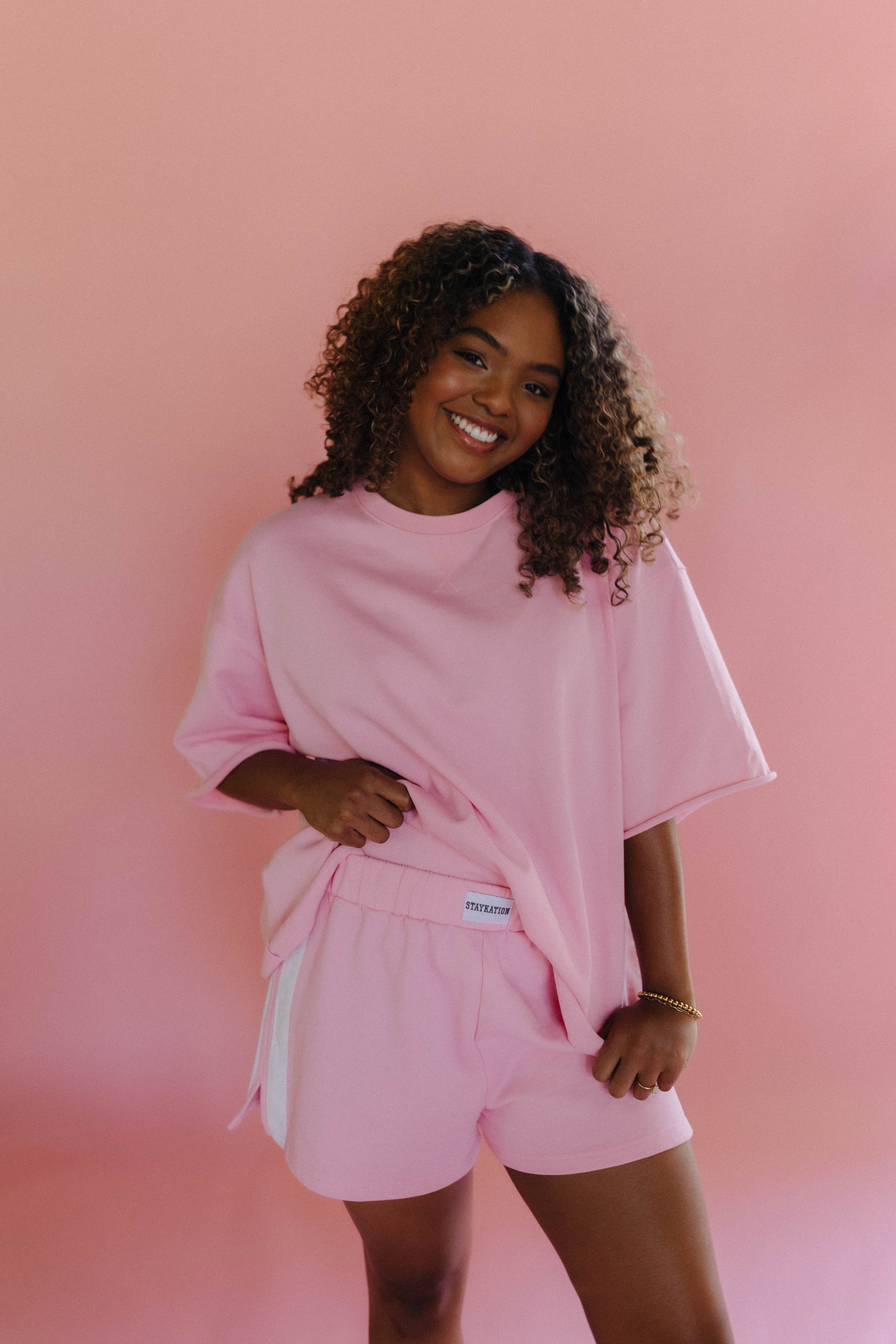Woman wearing a pink outfit with a small staykation logo on the waist on a pink background