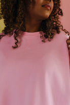 Person wearing a pink top with a blurred background showing the neckline detailing