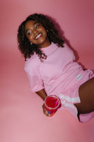 Woman in pink outfit holding a drink against a pink background