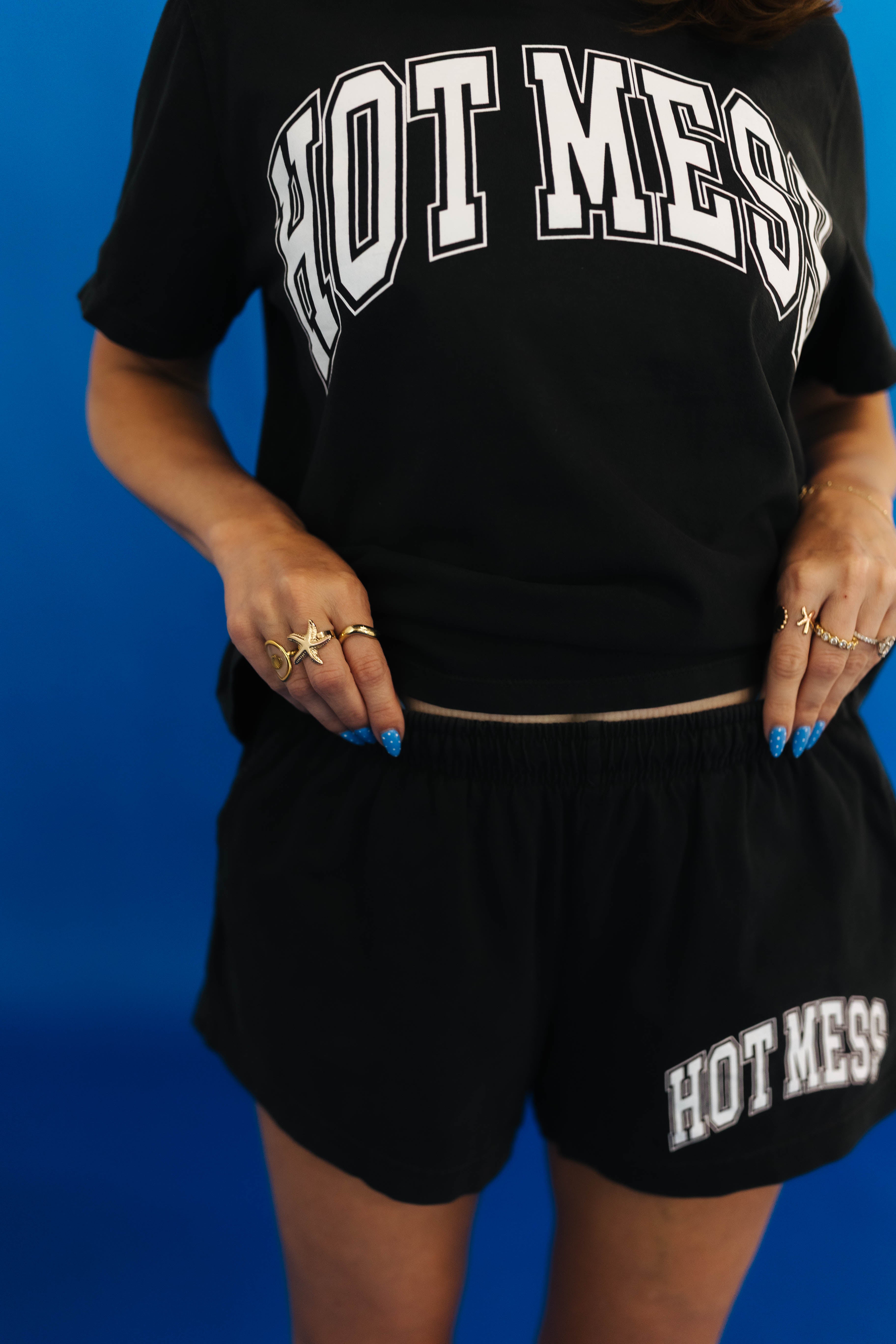 Person wearing a black 'HOT MESS' t-shirt and shorts on a blue background