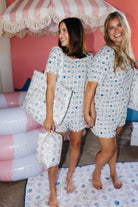 Two women wearing matching shell pajama sets standing under a striped canopy.