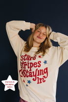 Person wearing a sweatshirt with 'stars stripes & staying in' text on a dark background