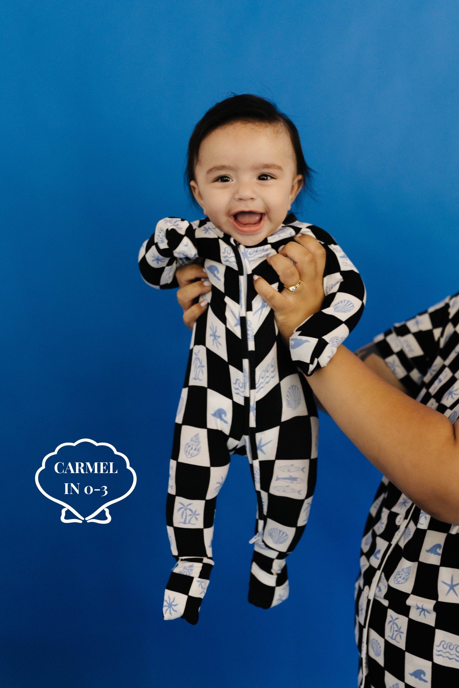 Baby in a black and white checkered outfit against a blue background size 0-3 months