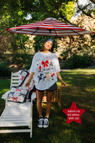 Woman standing under a red and white striped umbrella with a garden chair and decorative pillows in the background.