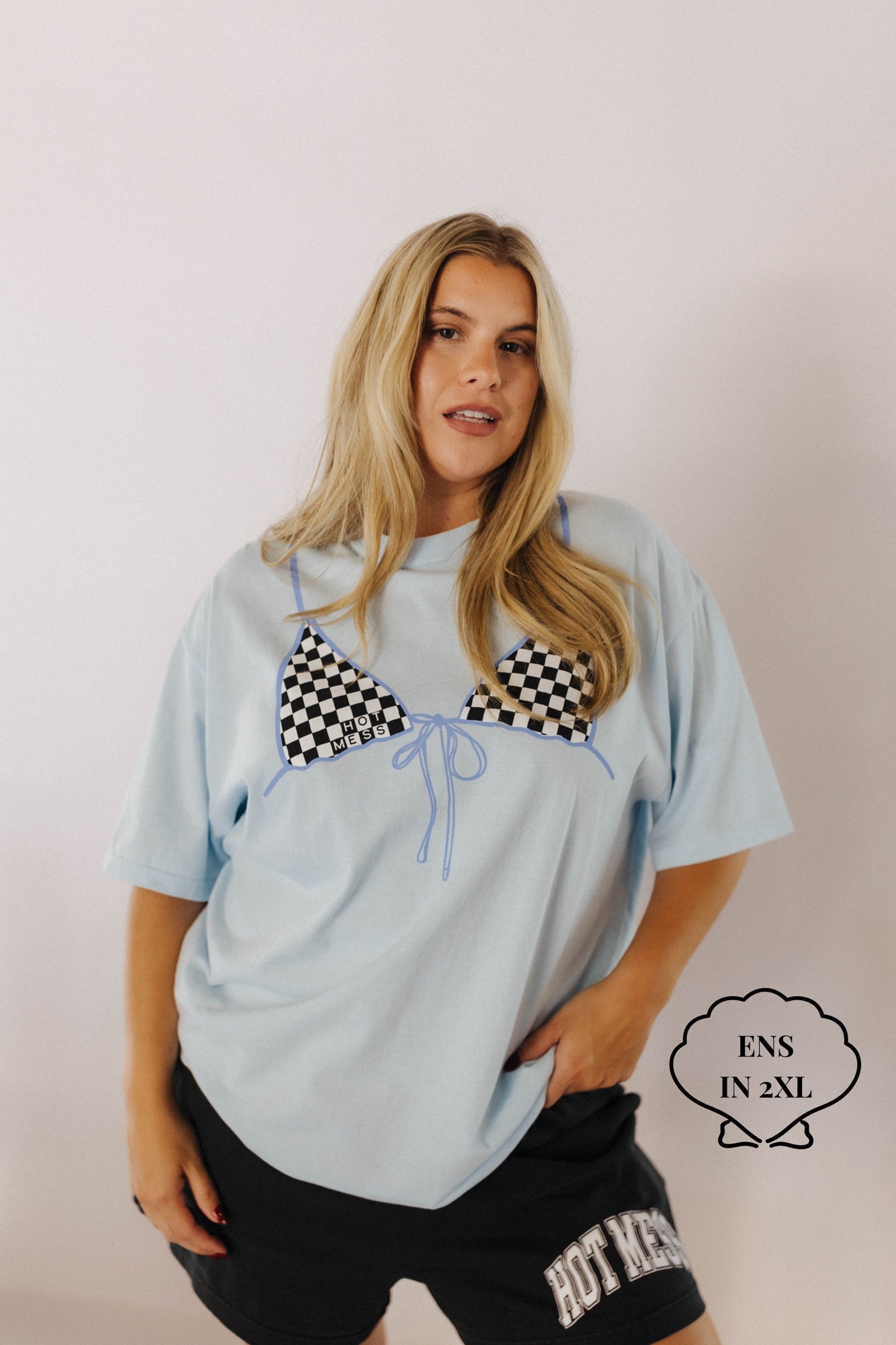 Woman wearing a light blue oversized t-shirt with a checkered design, standing against a plain background.
