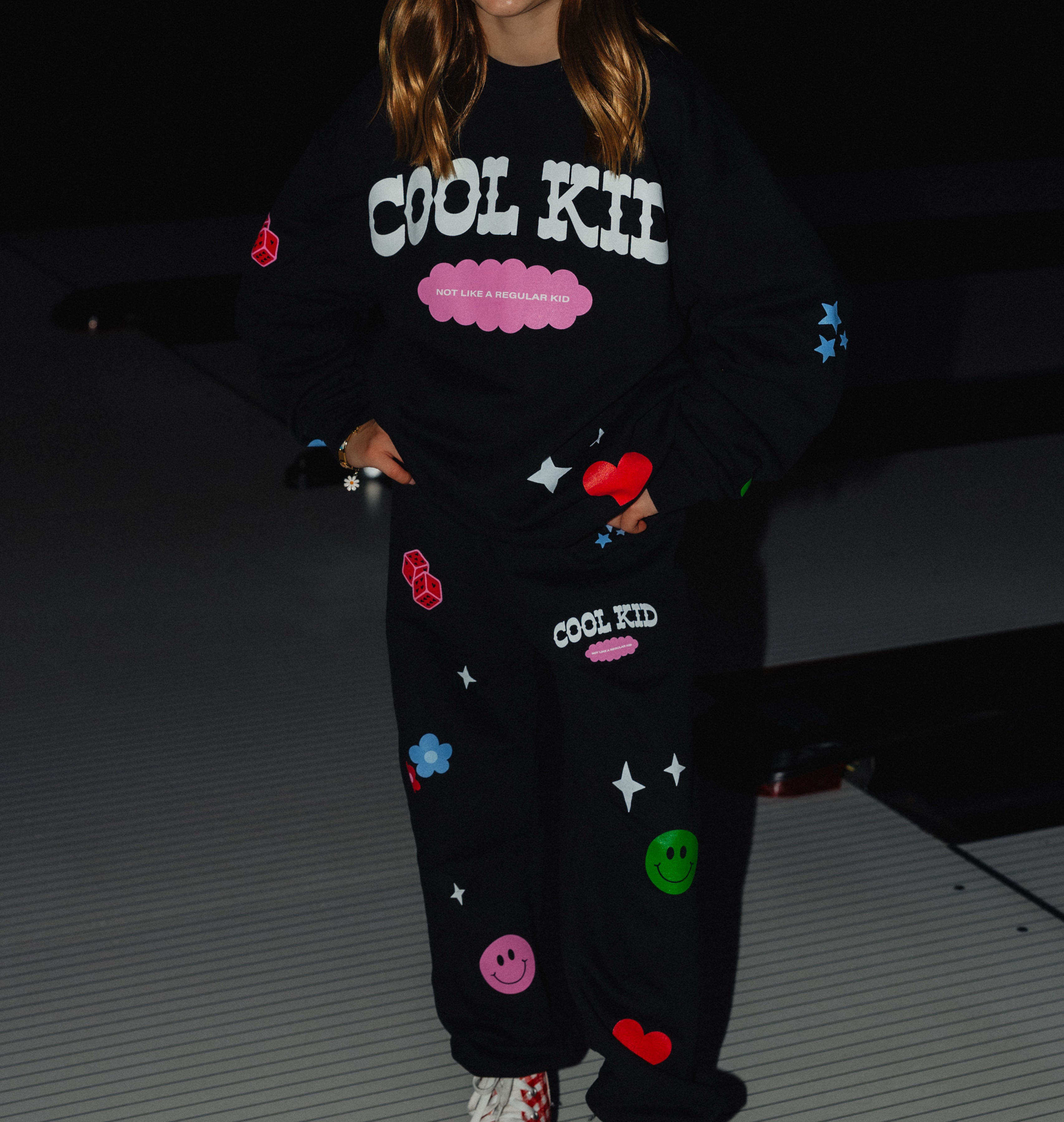 Sweatpants showing the cool kid logo and the not like a regular kid text along with the flowers, dice, smiley, hearts and flowers. 