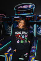 Krista in front of a bowling game at the arcade showing her cool mom sweatshirt that has bow, start, smiley, rose, and coffee cup.
