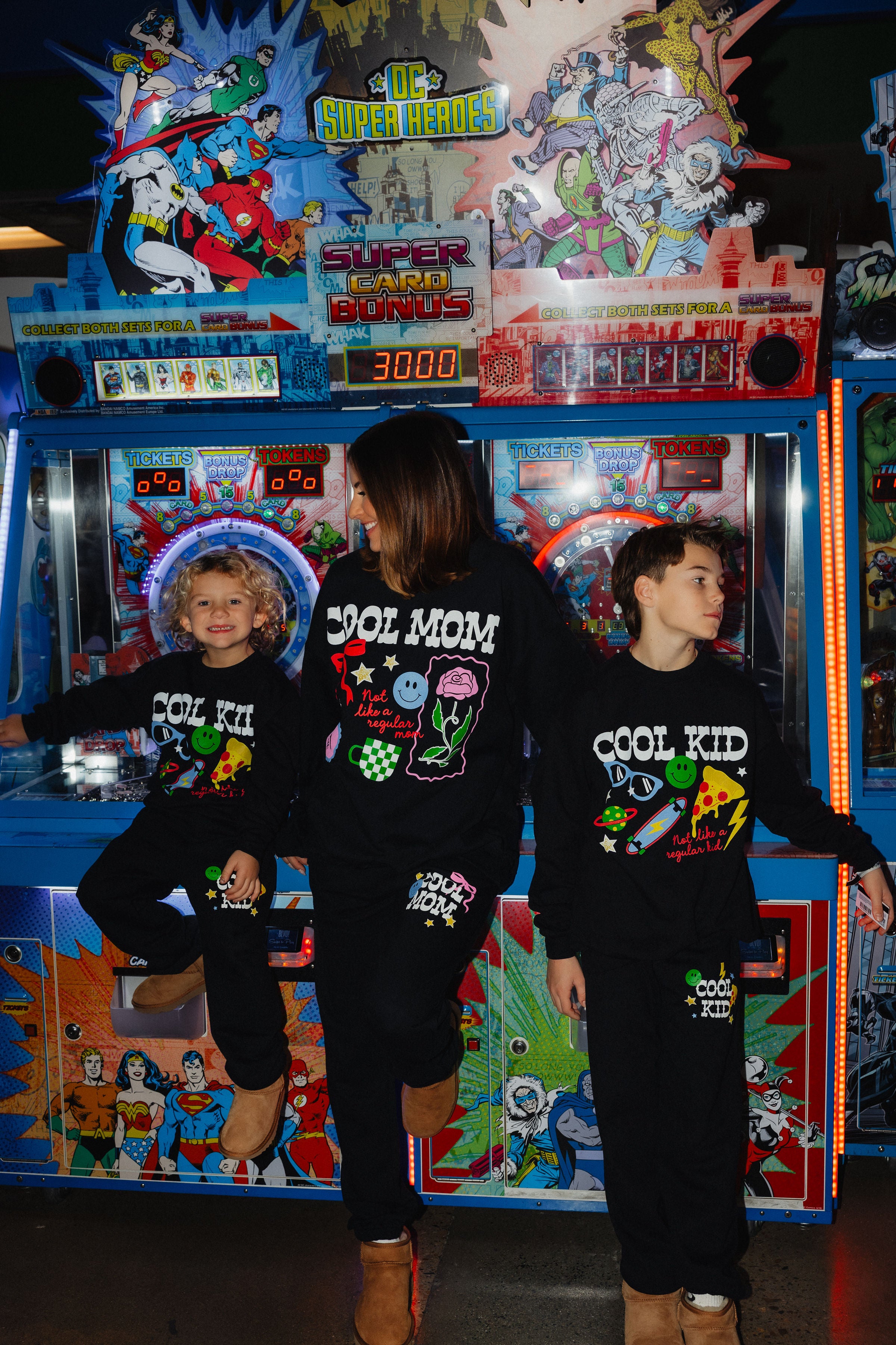 Kamp sitting on the arcade st smiling showing off his sweatset, Krista in the middle smiling at Kamp and boston on the side with a serious face showing off his set.