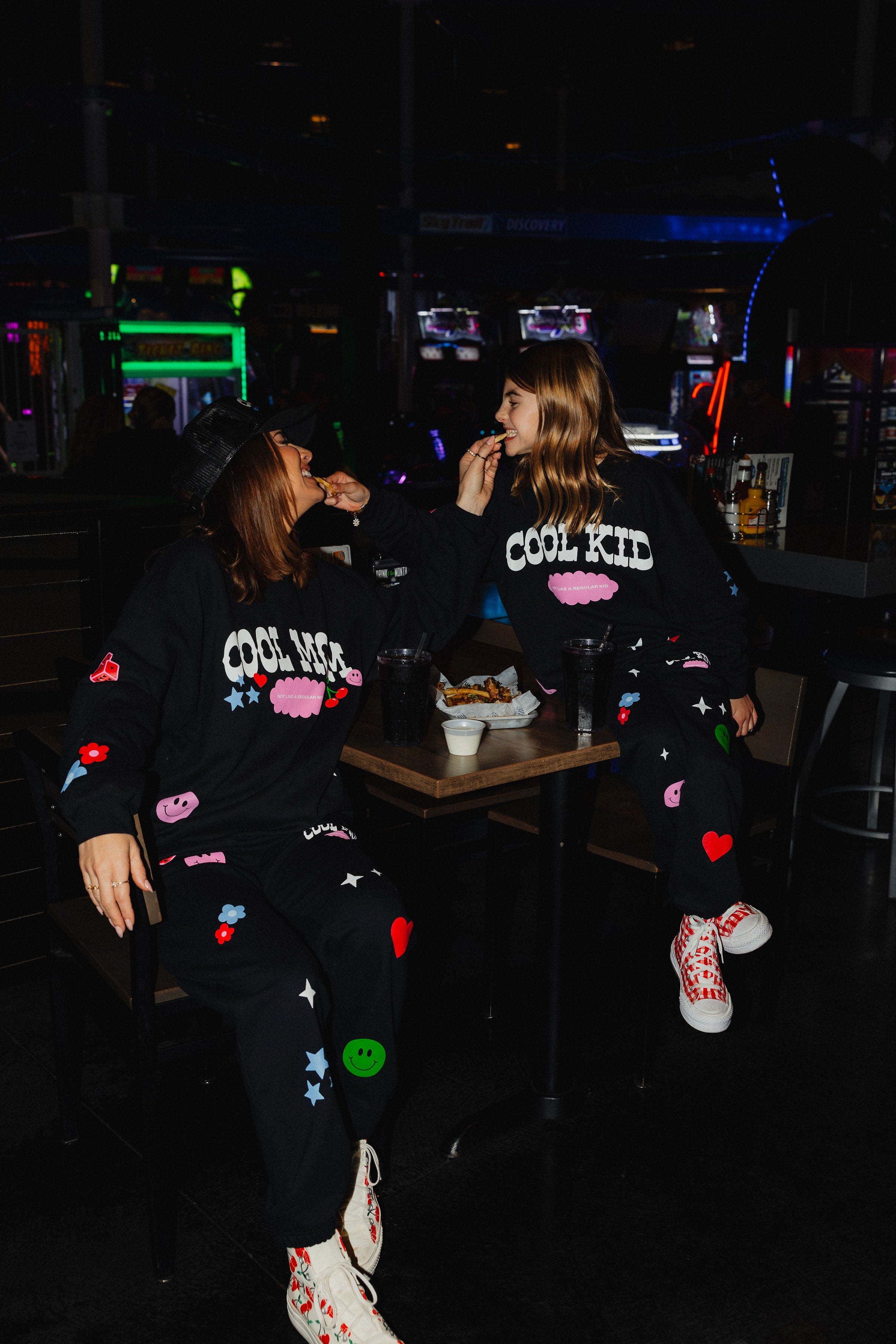 Krista sharing fries with kolly while sitting at the table showign their matching sweatsets. 