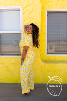 A woman posing in a yellow and white lemon-print pj in front of a bright yellow textured wall.